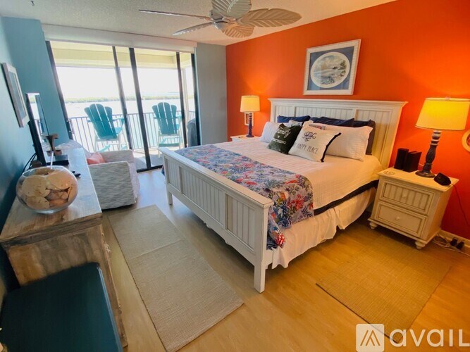 A bedroom with a large bed, a ceiling fan, and a balcony with chairs.