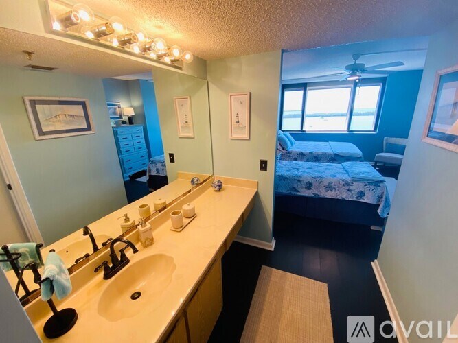 A bathroom with a vanity, mirror, and a bedroom in the background.
