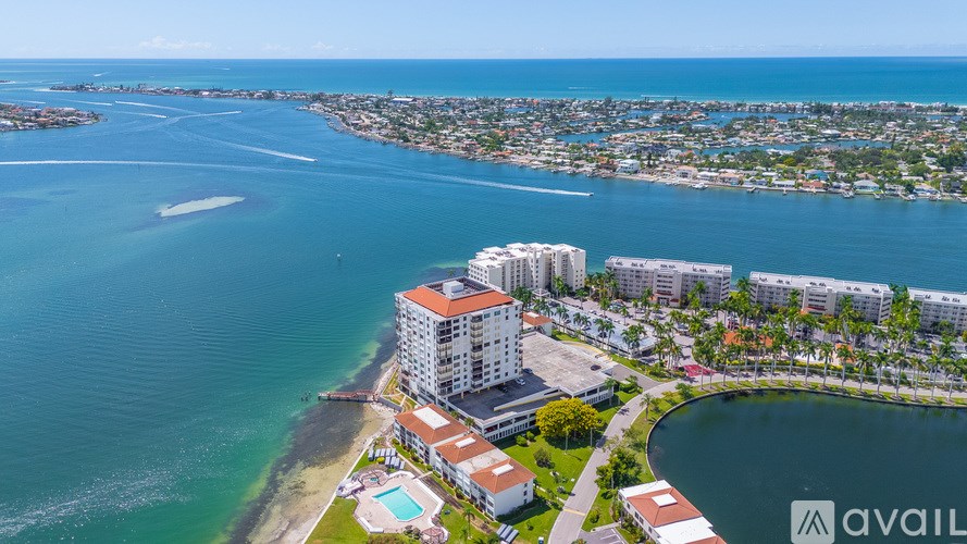 A large white building with a red roof is situated on the edge of a body of water.