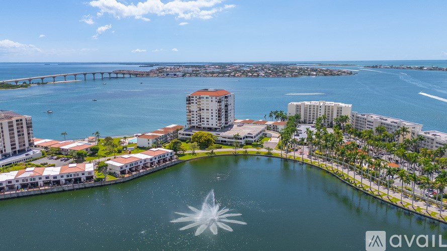 A fountain in the middle of a body of water with buildings and a bridge in the background.