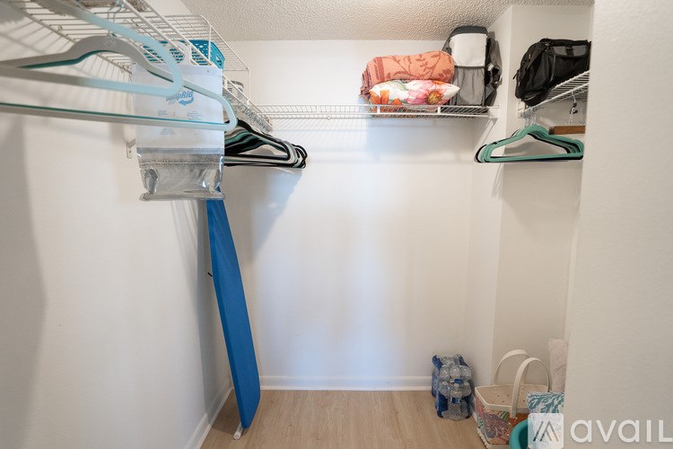 A small closet with clothes hanging and bags on the floor.