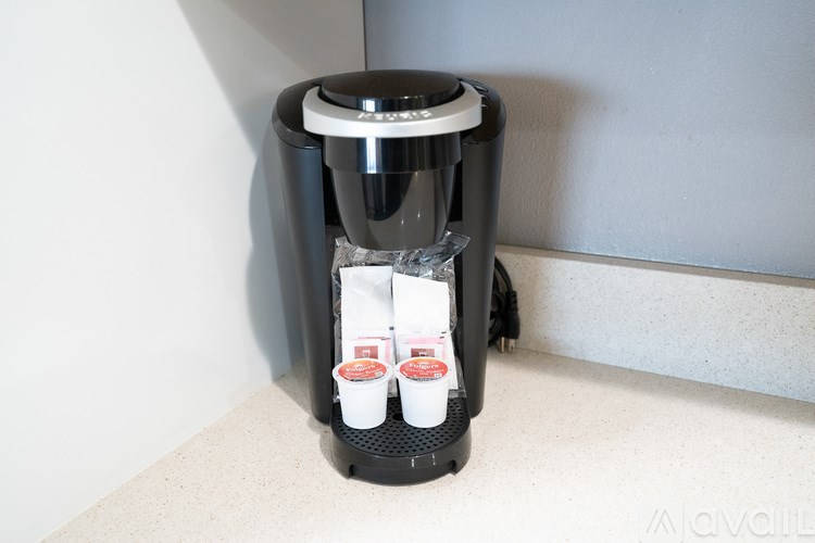 A coffee maker with two cups of coffee in front of it.