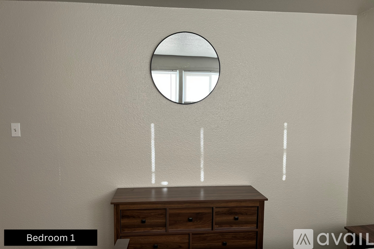 A round mirror hangs on a wall above a wooden dresser in Bedroom 1.