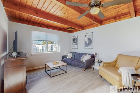 A living room with a yellow sofa, a wooden dresser, and a ceiling fan.