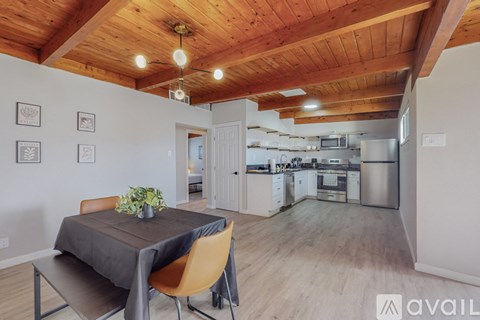 A dining area with a table and chairs in the foreground and a kitchen in the background.