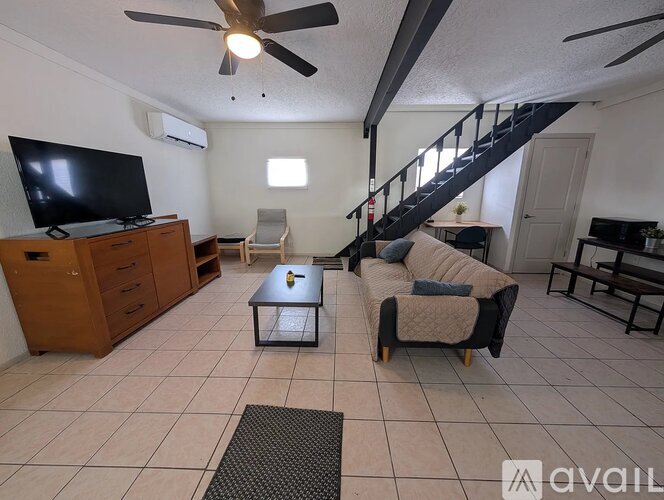 A living room with a television, a couch, and a staircase.