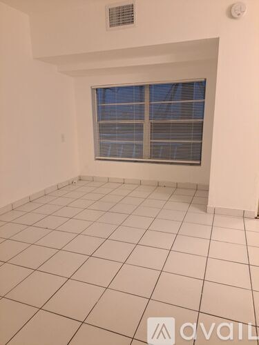 A room with a window covered by blinds and tiled flooring.