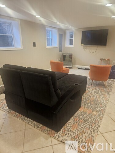 A black couch sits in a living room with a television mounted on the wall.
