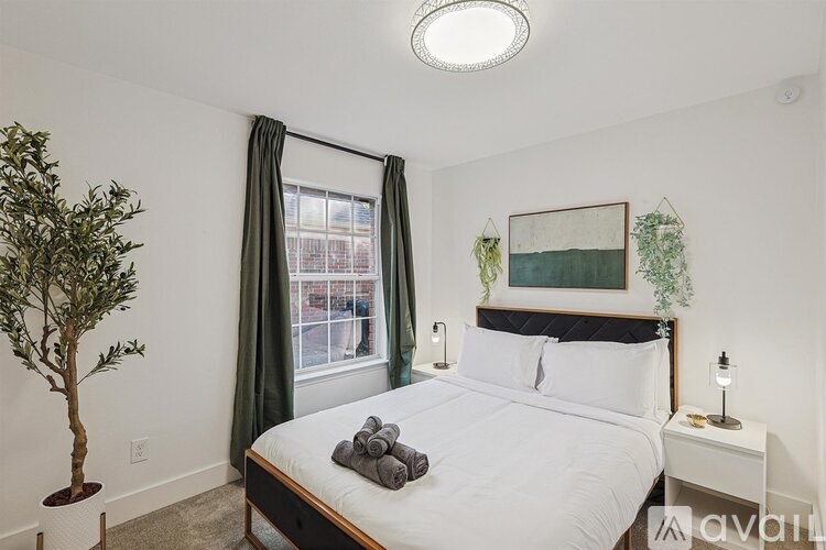 A bedroom with a bed, nightstand, and a potted plant.