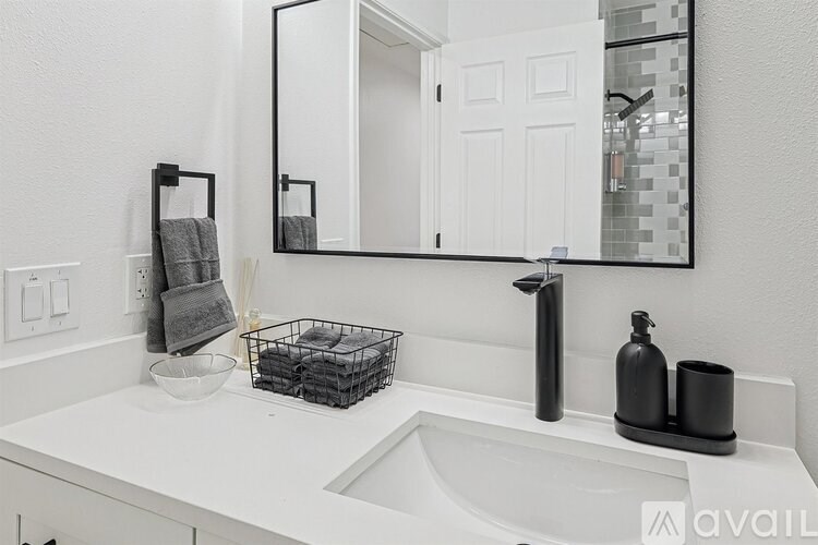 A bathroom sink with a mirror above it and a basket of towels to the left.