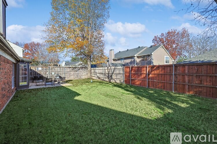 A backyard with a fence and a tree with yellow leaves.
