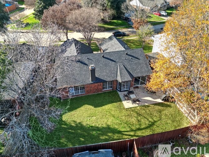 A house with a black roof and a chimney is surrounded by a green lawn and trees.
