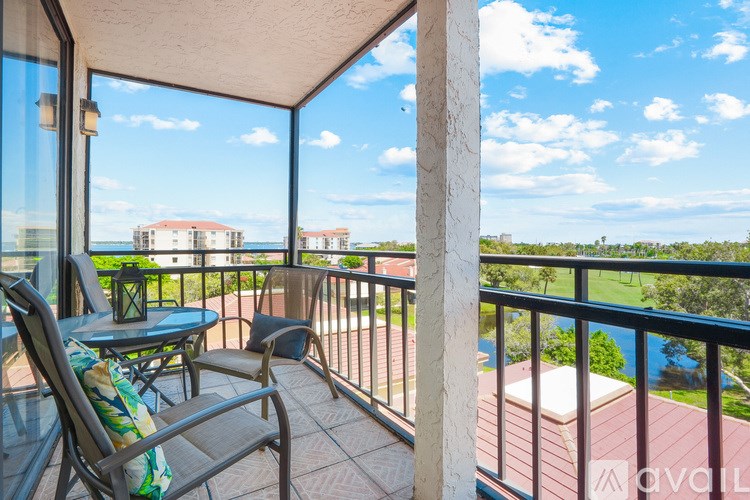 A balcony with a table and chairs overlooking a pool and buildings.