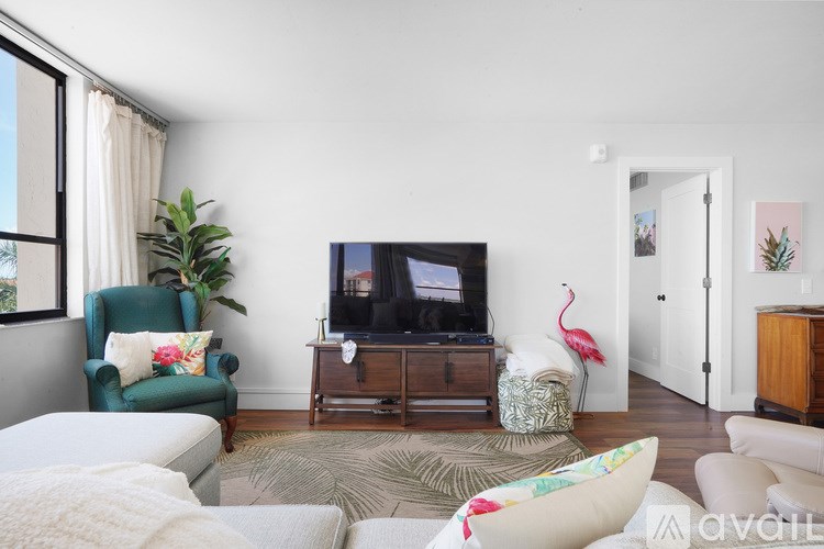 A living room with a green armchair, a white sofa, a wooden entertainment center, and a TV on the wall.