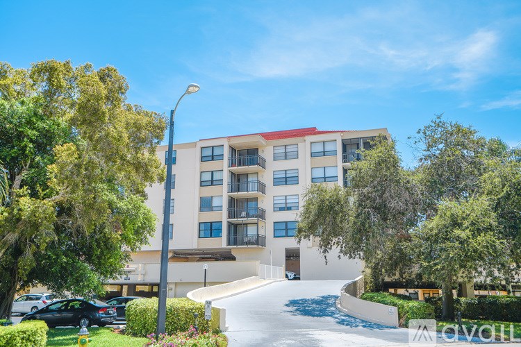 A modern building with a red roof is surrounded by greenery and a clear blue sky.