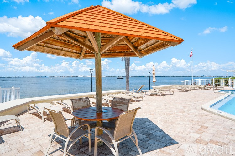 A table with chairs and an umbrella is on a patio overlooking the water.