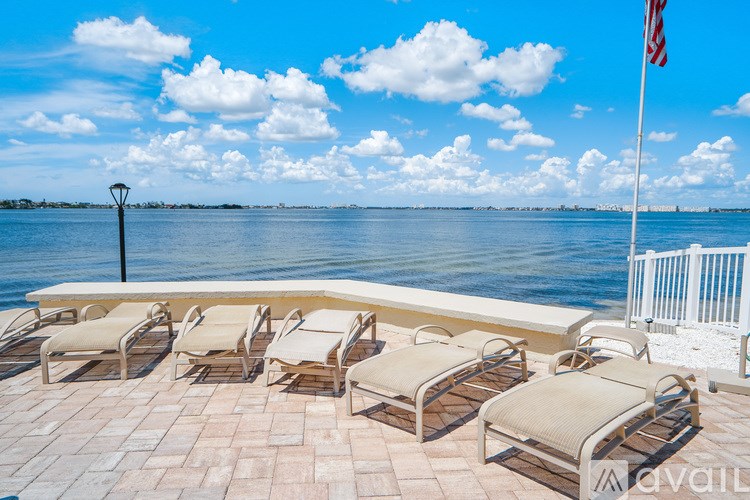 A row of sun loungers are on a patio overlooking a body of water.