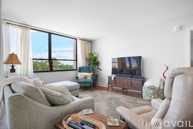A living room with a grey couch, a white armchair, a wooden coffee table, a television, and a window with a view of the outdoors.