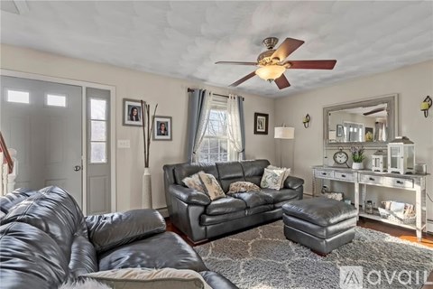A living room with a black leather couch and a fan on the ceiling.