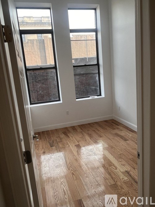 A room with a wooden floor and a window overlooking a fence.