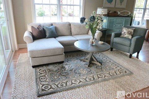 A living room with a white couch, a grey armchair, and a round table with a vase of flowers on it.