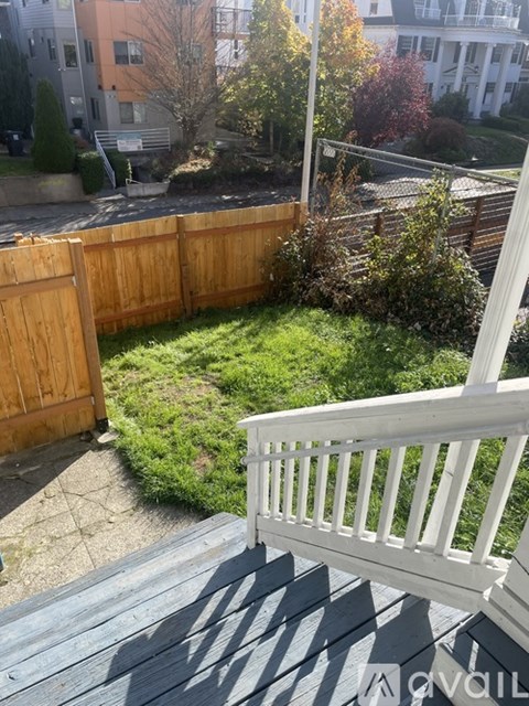 A wooden deck with a white railing overlooks a backyard with a wooden fence and a small tree.