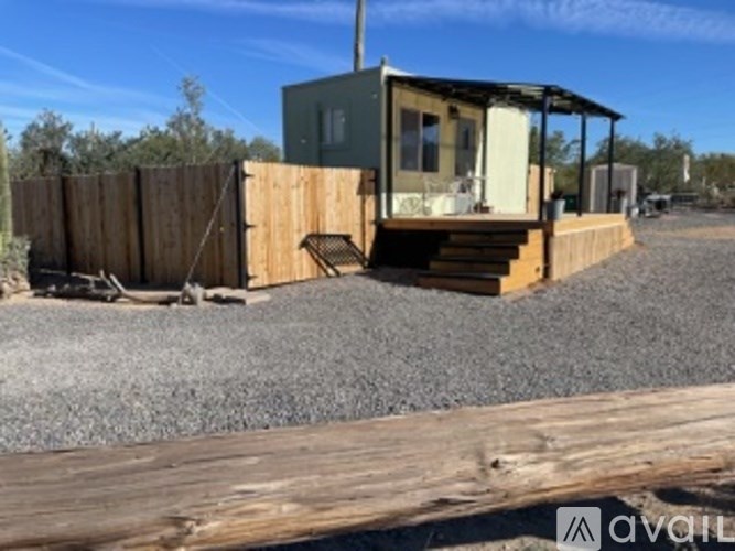 A small house with a porch is situated on a gravel area.