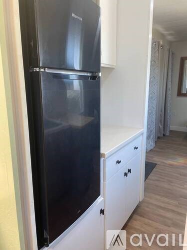 A black refrigerator is in a kitchen with white cabinets.