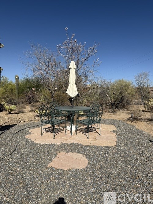 A table and chairs set up under a white umbrella in a gravel area.
