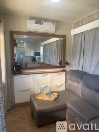 A living room with a grey couch, a grey ottoman, a mirror, and a white cabinet.