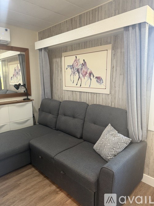 A grey sofa with a pillow and a painting of horses on the wall.