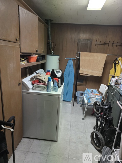 A small, cluttered laundry room with a washer and dryer, a mop, and a wheelchair.