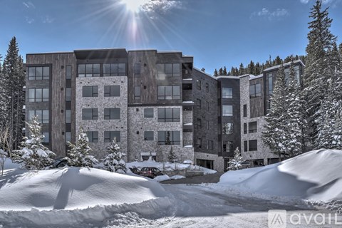 A large building with a lot of windows is surrounded by snow and trees.