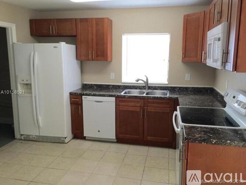 A kitchen with a white fridge, brown cabinets, and a black countertop.