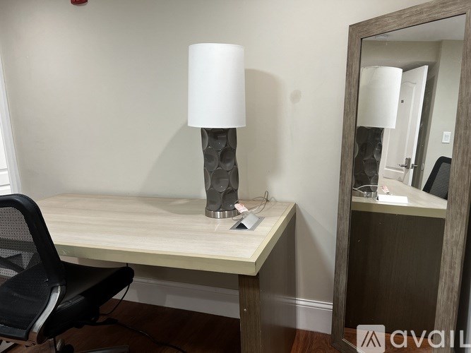 A desk with a chair and a lamp in front of a mirror.