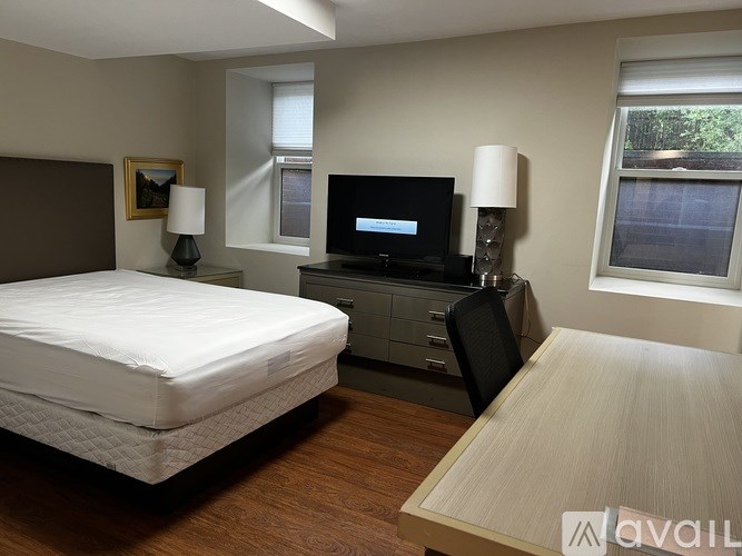 A bedroom with a bed, a desk with a chair, and a television.