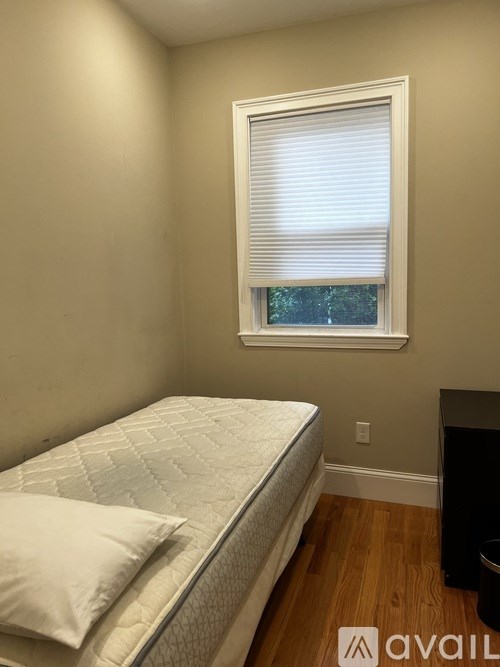 A bedroom with a bed, a window with blinds, and a black object on the floor.