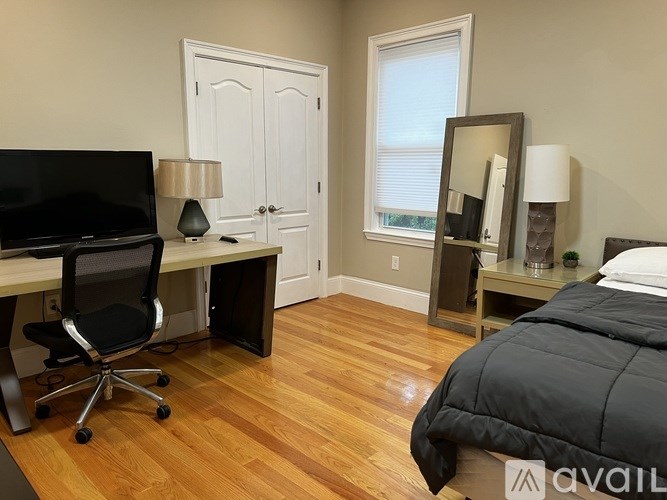 A bedroom with a bed, desk, chair, and a mirror.