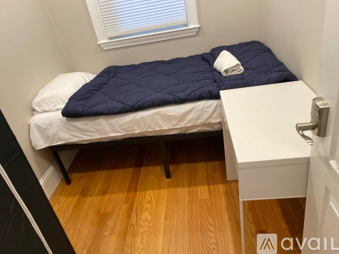 A small bedroom with a bed, a pillow, a blanket, a nightstand, and a window.