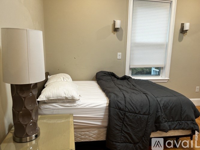 A bedroom with a bed covered in a black comforter and a lamp on a nightstand.