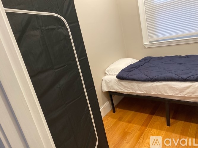 A bed with a blue blanket and a white pillow is in a room with a wooden floor and a white wall.