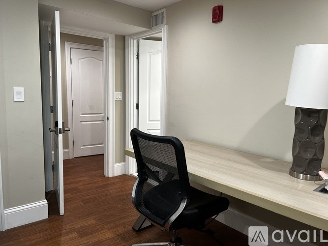 A black chair is in front of a white bench with a lamp on it.