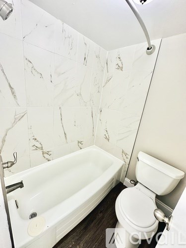 A white toilet sits next to a bathtub in a bathroom with marble walls.