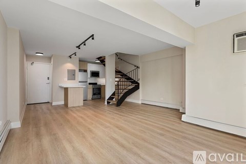 A spacious room with wooden flooring and a staircase with a metal railing.