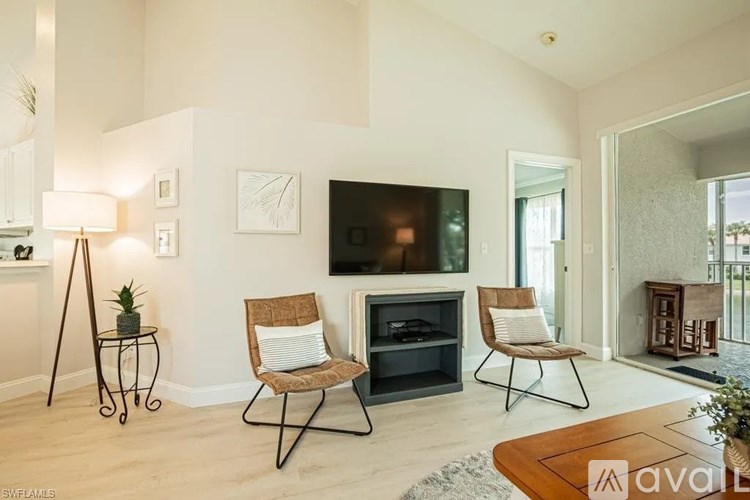 A living room with a flat screen TV mounted on the wall, two chairs, and a small table with a plant on it.