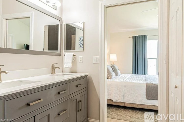 A bathroom with a sink, mirror, and a bedroom in the background.