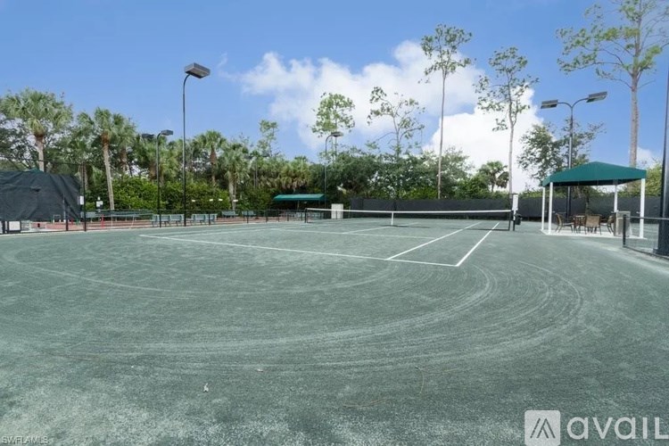 A tennis court with a green roofed pavilion and trees in the background.