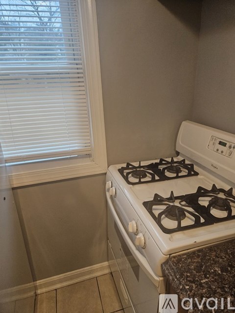 A white gas stove in a kitchen with a window covered in blinds.