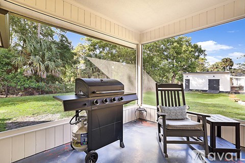 A grill is on a patio with a chair and table.