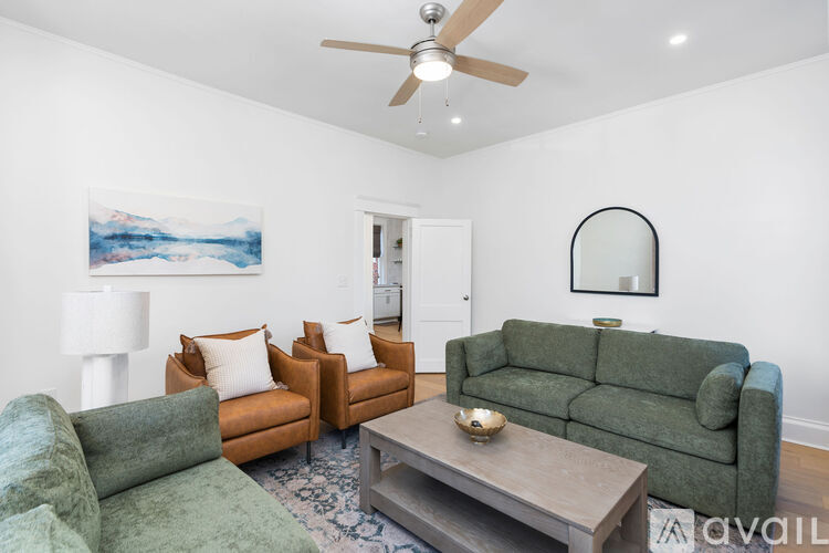 A living room with a green couch, a brown chair, and a painting of a mountain scene on the wall.